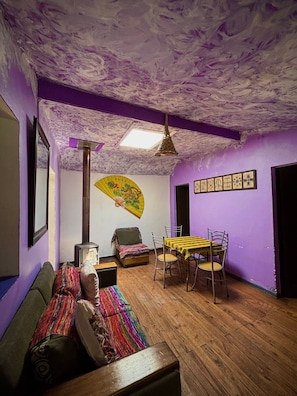 A room with a wooden floor, a sofa, a table with chairs, a fan, and a ceiling with a textured finish.