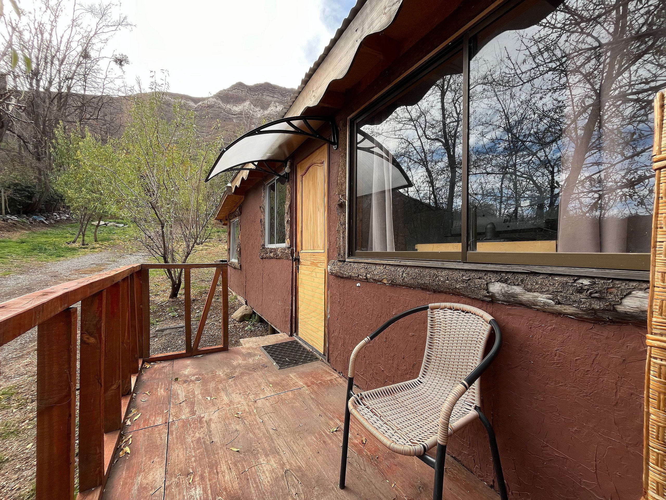 Una terraza de madera con una silla de mimbre, una ventana que ofrece vistas a las montañas y una barandilla de madera.