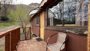Una terraza de madera con una silla de mimbre, una ventana que ofrece vistas a las montañas y una barandilla de madera.