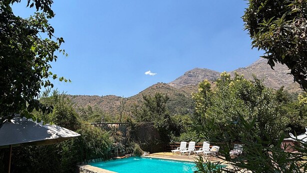 A swimming pool surrounded by a stone wall, with a view of mountains in the background. - Oceana Suites San San José de Maipo II (San Alfonso)