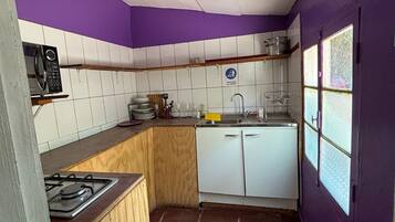 Cocina compacta con estufa a gas, armarios blancos, un lavamanos y una ventana con vistas.