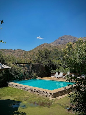 A swimming pool with a stone border, surrounded by greenery and white lounge chairs.