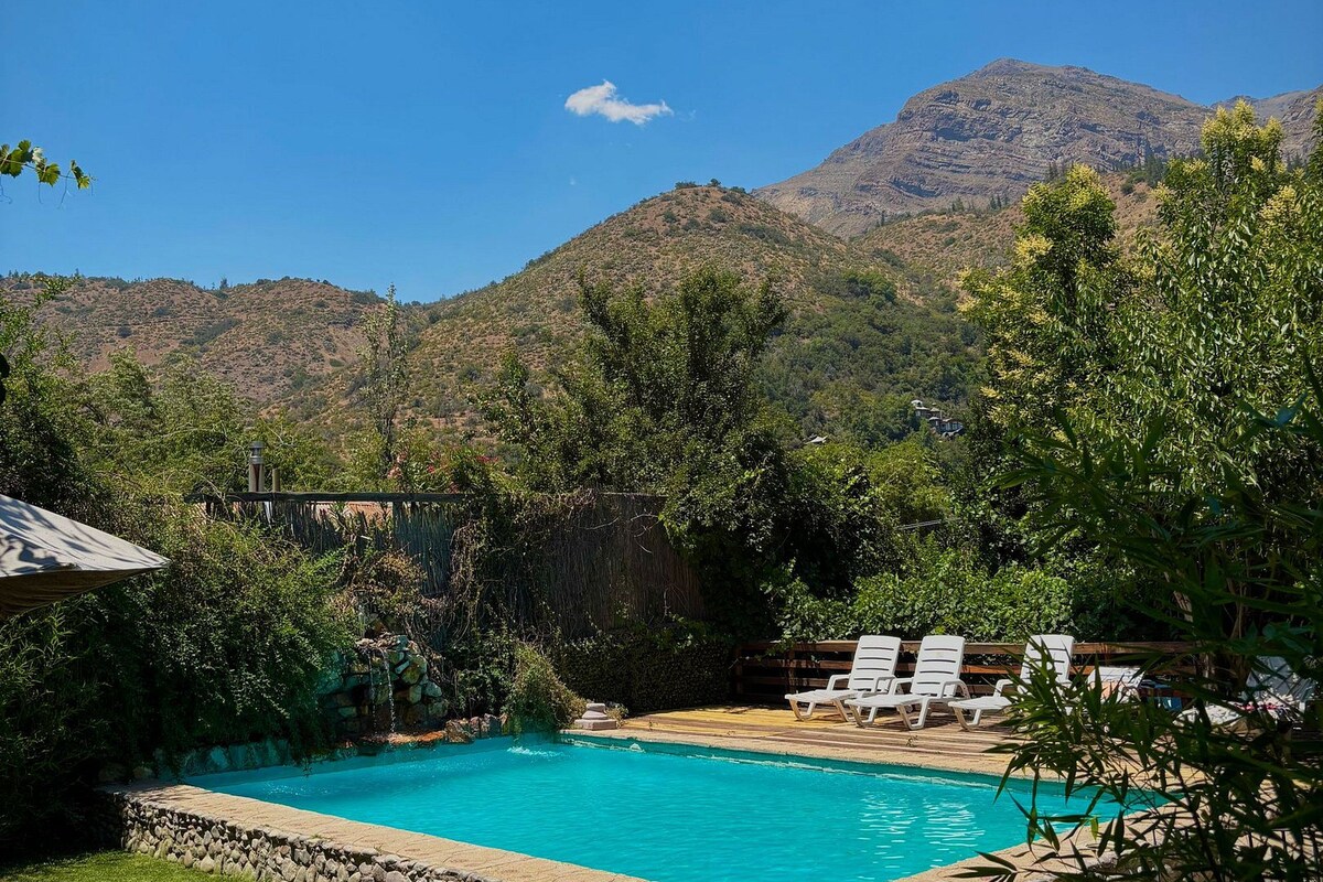 A swimming pool with a stone border, surrounded by greenery and white lounge chairs.