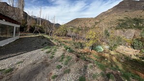 A mountainous landscape with a building featuring large windows, surrounded by trees and a gravel path. - Oceana Suites San San José de Maipo II (San Alfonso)