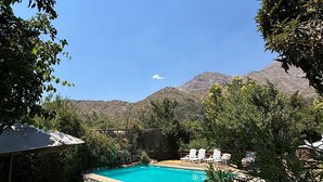 A swimming pool surrounded by a stone wall, with a view of mountains in the background. - Oceana Suites San San José de Maipo II (San Alfonso)