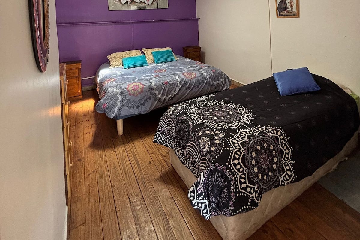 Ein Schlafzimmer mit zwei Betten, Holzboden, Deckenventilator und einer Wandleuchte.
