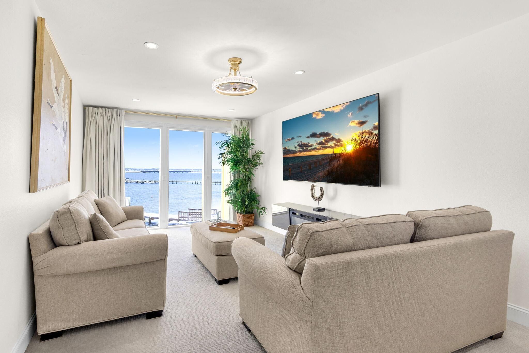 A modern living room with a sofa set, a flat-screen TV, and a large window overlooking a body of water.