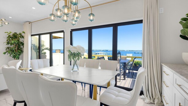 Een moderne eetruimte met een grote tafel, witte stoelen en uitzicht op zee.