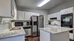 A kitchen with white cabinets, a stainless steel refrigerator, a dishwasher, a coffee maker, and an oven.
