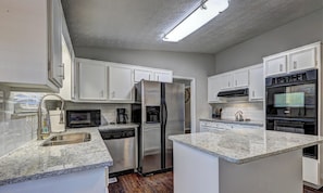 A kitchen with white cabinets, a stainless steel refrigerator, a dishwasher, a coffee maker, and an oven. - The Red Ranch - Near Six Flags & ATL Attractions! (Douglasville)