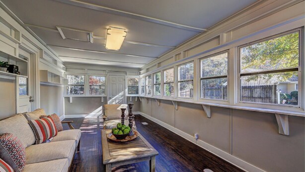 A long room with a sofa, a table with fruit, and large windows.
