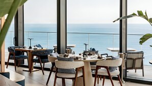 Un comedor moderno con vista al mar, que incluye una mesa redonda, sillas y una lámpara colgante.