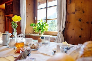 Innenansicht einer Holzhütte mit einem gedeckten Frühstückstisch, einer gelben Blume und einem Fenster mit Vorhängen.
