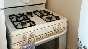 A kitchen with a stove, oven, spice rack, and hanging utensils. - Fully Furnished Corporate Rental - 2 Kitchens + Private Suite - 30+ Day Stays (Barberton)