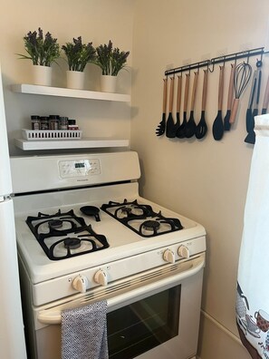 A kitchen with a stove, oven, spice rack, and hanging utensils. - Fully Furnished Corporate Rental - 2 Kitchens + Private Suite - 30+ Day Stays (Barberton)