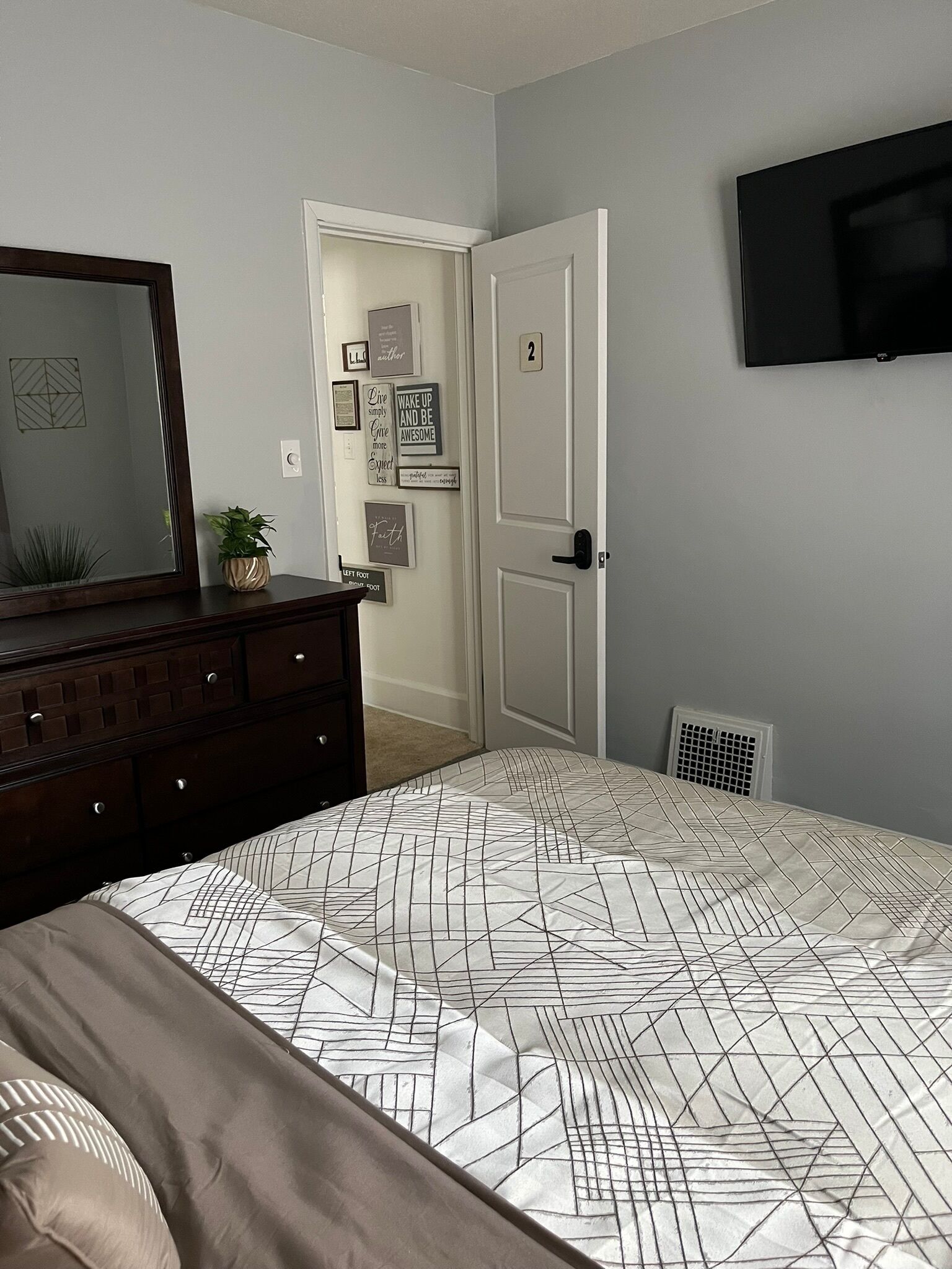 A bedroom with a bed, dresser, wall-mounted TV, and motivational wall art.