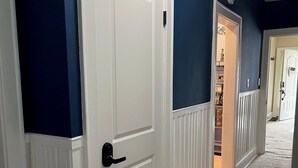 A hallway with a white door, a blue wall, and a carpeted floor. - Fully Furnished Corporate Rental - 2 Kitchens + Private Suite - 30+ Day Stays (Barberton)