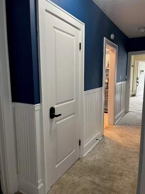A hallway with a white door, a blue wall, and a carpeted floor. - Fully Furnished Corporate Rental - 2 Kitchens + Private Suite - 30+ Day Stays (Barberton)