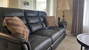 A black leather sofa with two throw pillows, a lamp, and a small table with a plant. - Fully Furnished Corporate Rental - 2 Kitchens + Private Suite - 30+ Day Stays (Barberton)