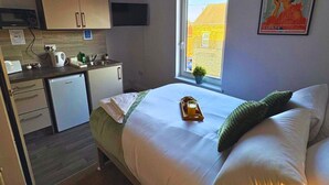 A compact room with a bed, a small kitchenette, a window with a view, and a vintage poster on the wall. - Contemporary City Studio 4 - Contractor's & Traveller's Accommodation (Peterborough)