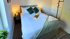 A neatly made bed with pillows, a tray with fruits and a drink, a bedside lamp, and a coat rack. - Contemporary City Studio 4 - Contractor's & Traveller's Accommodation (Peterborough)