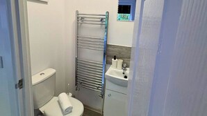 A compact bathroom with a toilet, a towel rack, a sink, and a window. - Contemporary City Studio 4 - Contractor's & Traveller's Accommodation (Peterborough)