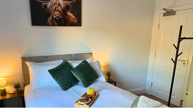 A hotel room with a bed, pillows, a tray with food and drink, a coat rack, and a painting of a bull on the wall. - Contemporary City Studio 4 - Contractor's & Traveller's Accommodation (Peterborough)
