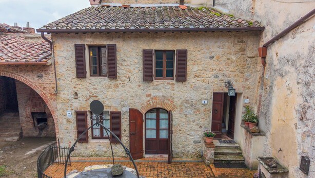 Un bâtiment en pierre avec un toit en tuiles, une porte centrale et une petite cour intérieure agrémentée d’une fontaine.