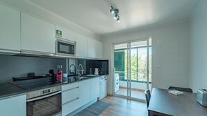 A modern kitchen with white cabinets, a microwave, a stove, and a sink. There is a dining area with a table and chairs. - Home Azores - Loreto Apartment (Ponta Delgada)