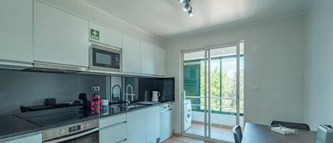 A modern kitchen with white cabinets, a microwave, a stove, and a sink. There is a dining area with a table and chairs.