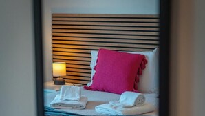 A neatly made bed with rolled towels, a pink pillow, and a striped blanket. - Home Azores - Loreto Apartment (Ponta Delgada)