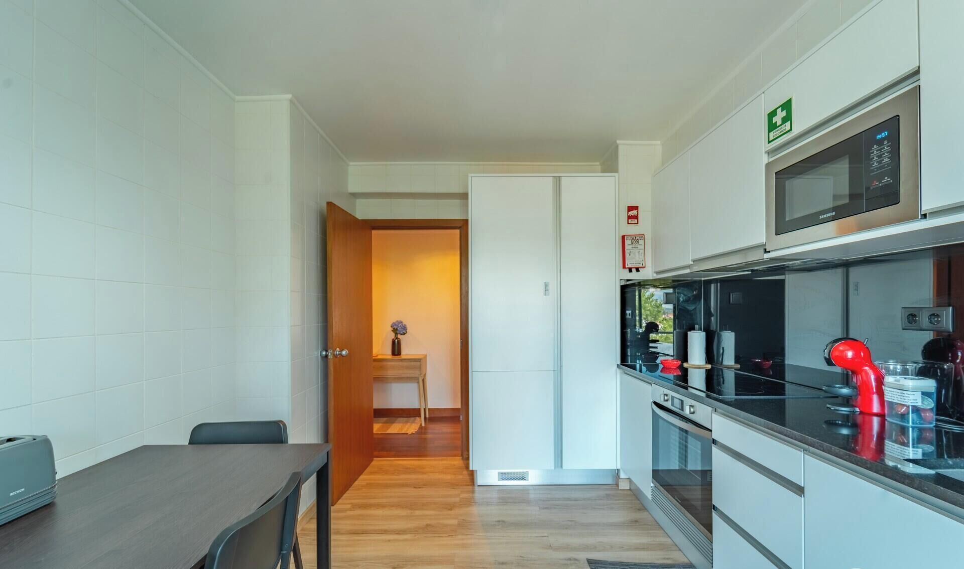Una cocina moderna con microondas, horno y hervidor rojo. Hay un comedor con mesa y sillas.