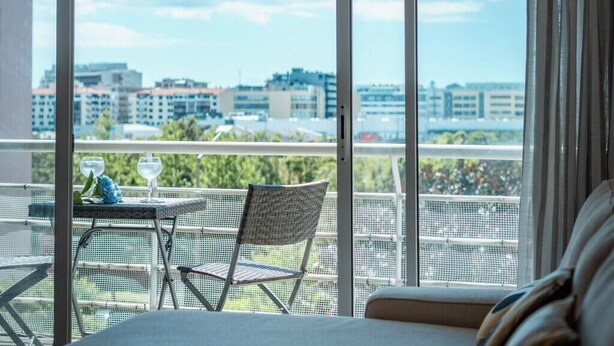 A balcony with a table and chairs, a hanging light fixture, and a view of buildings and greenery. - Home Azores - Loreto Apartment (Ponta Delgada)