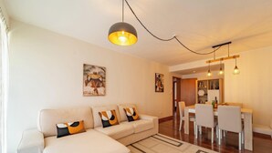 A modern living room with a sofa, dining table, and hanging lights. - Home Azores - Loreto Apartment (Ponta Delgada)