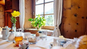 L’intérieur d’un chalet en bois, avec une table de petit-déjeuner dressée, une fleur jaune et une fenêtre avec des rideaux.