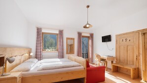 Une chambre avec un lit en bois, une chaise rouge, une armoire en bois, une petite table et un téléviseur fixé au mur.
