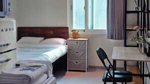 A bedroom with a bed, a desk, a chair, a nightstand, a dresser, a window with curtains, and a potted plant. - U Stay Hostel Gasan (Seoul)