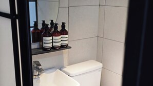 A bathroom with a white sink, a toilet, and a shelf with bottles of body wash and shampoo. - U Stay Hostel Gasan (Seoul)