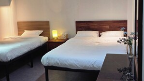 A hotel room with two single beds, a nightstand with a lamp, a vase with flowers, and a wooden headboard. - U Stay Hostel Gasan (Seoul)