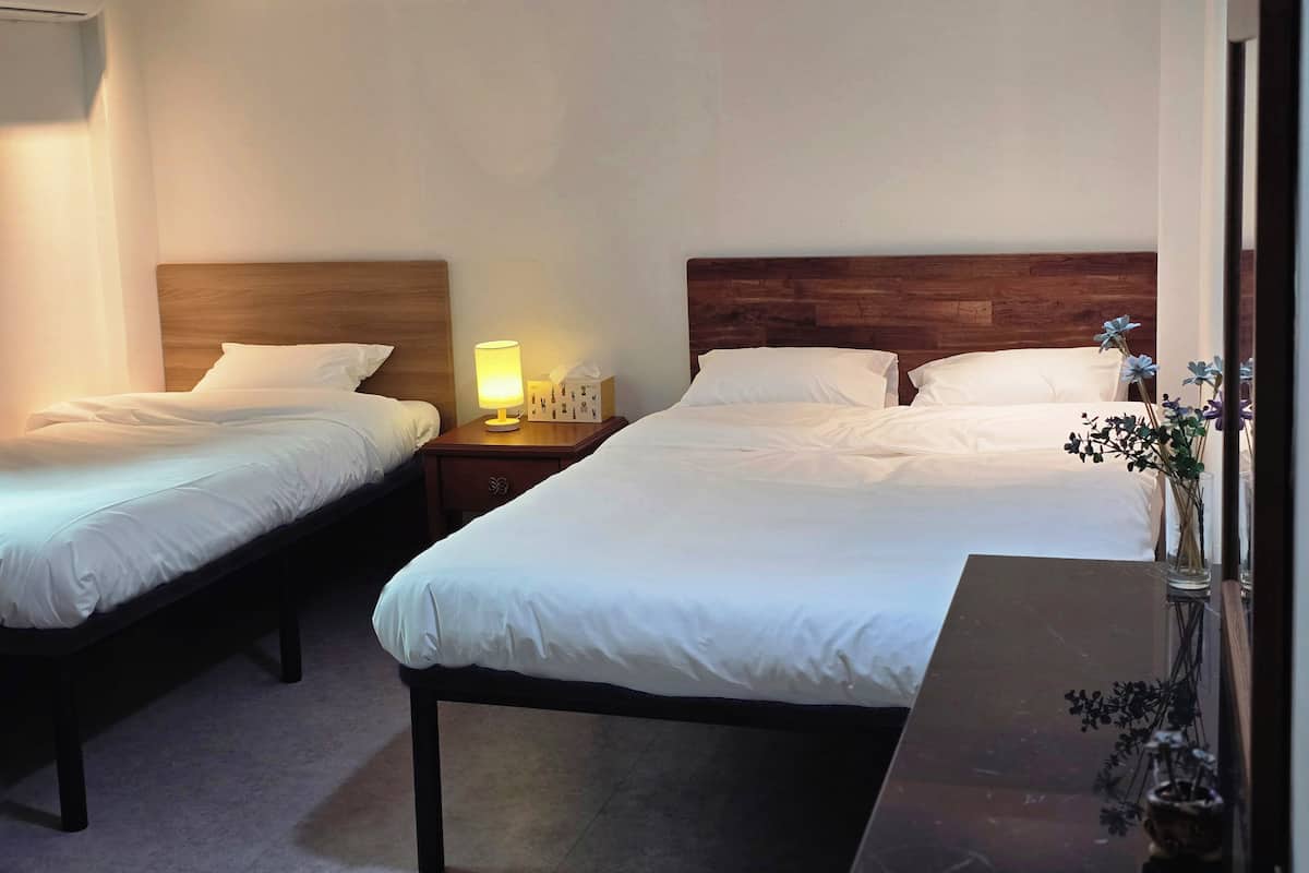 A hotel room with two single beds, a nightstand with a lamp, a vase with flowers, and a wooden headboard.