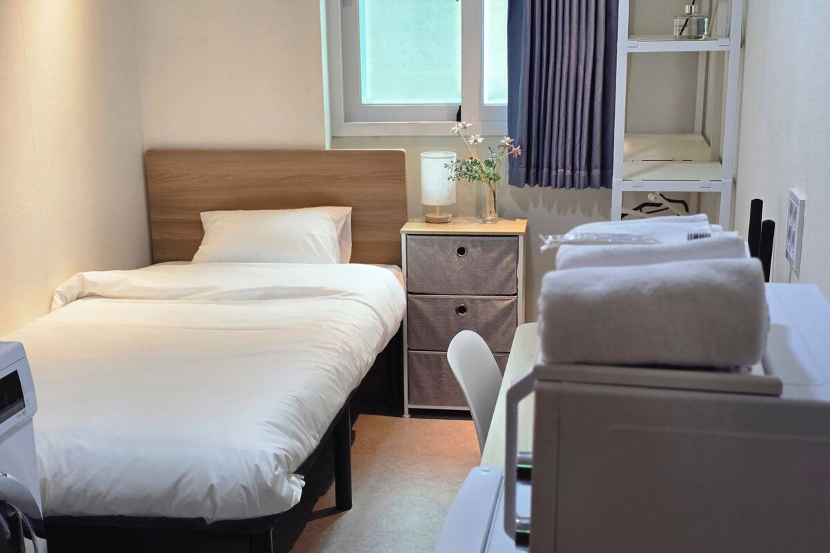 A hotel room with a bed, bedside table, lamp, and a chair.