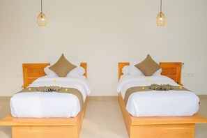 Una habitación con dos camas iguales, cada una con cabecero de madera, ropa de cama blanca y almohada marrón. Hay dos lámparas colgantes en el techo.