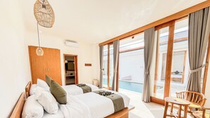 A bedroom with a large bed, a wooden wardrobe, a small table, and a view of a pool.