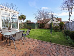 A patio with a table and chairs, a green shed, and a well-maintained lawn. - The Nook (Whitby)