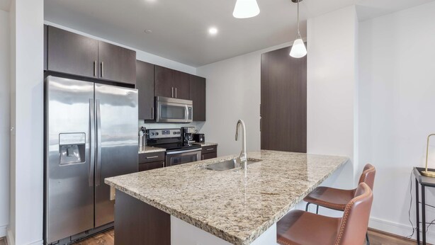A modern kitchen with a stainless steel refrigerator, a microwave, a sink, and granite countertops. - Modern Apt Heart of Seaport (Boston, MA)
