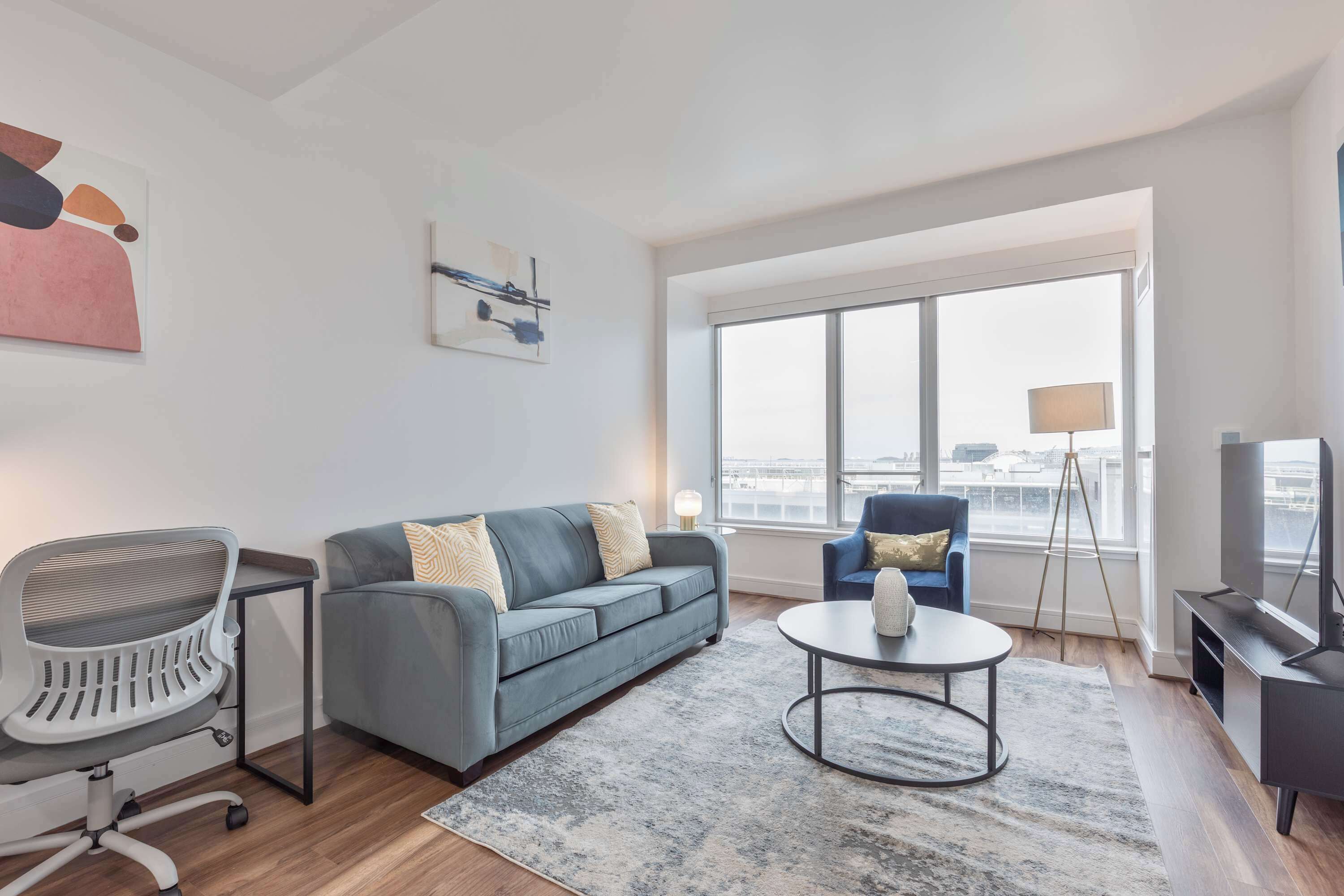 A modern living room with a grey sofa, a white office chair, a coffee table, and a TV.