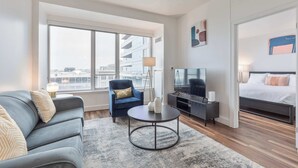 A modern hotel room with a sofa, a chair, a round coffee table, a TV, and a bed. - Modern Apt Heart of Seaport (Boston, MA)