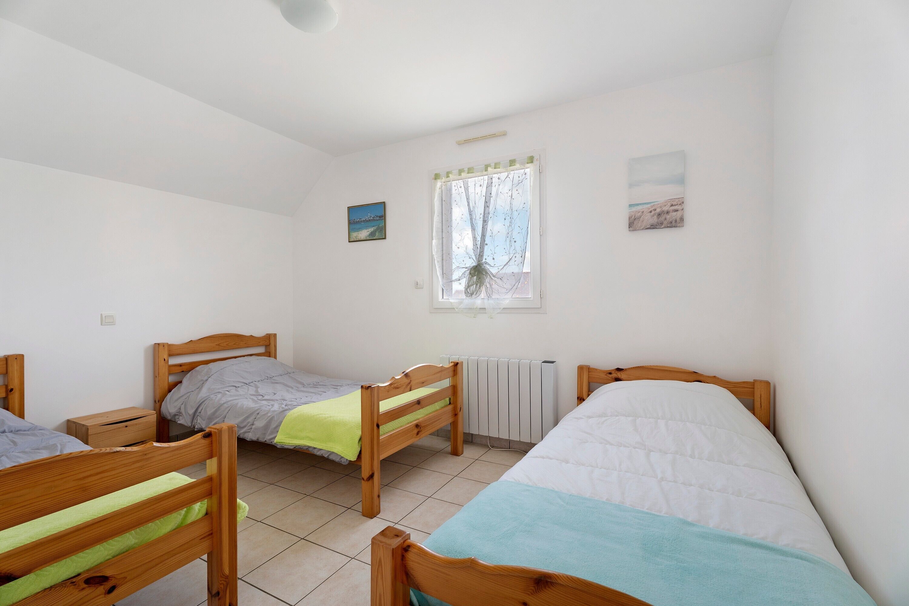 Une pièce comprenant trois lits en bois, un radiateur, une fenêtre avec un rideau et deux tableaux accrochés au mur.