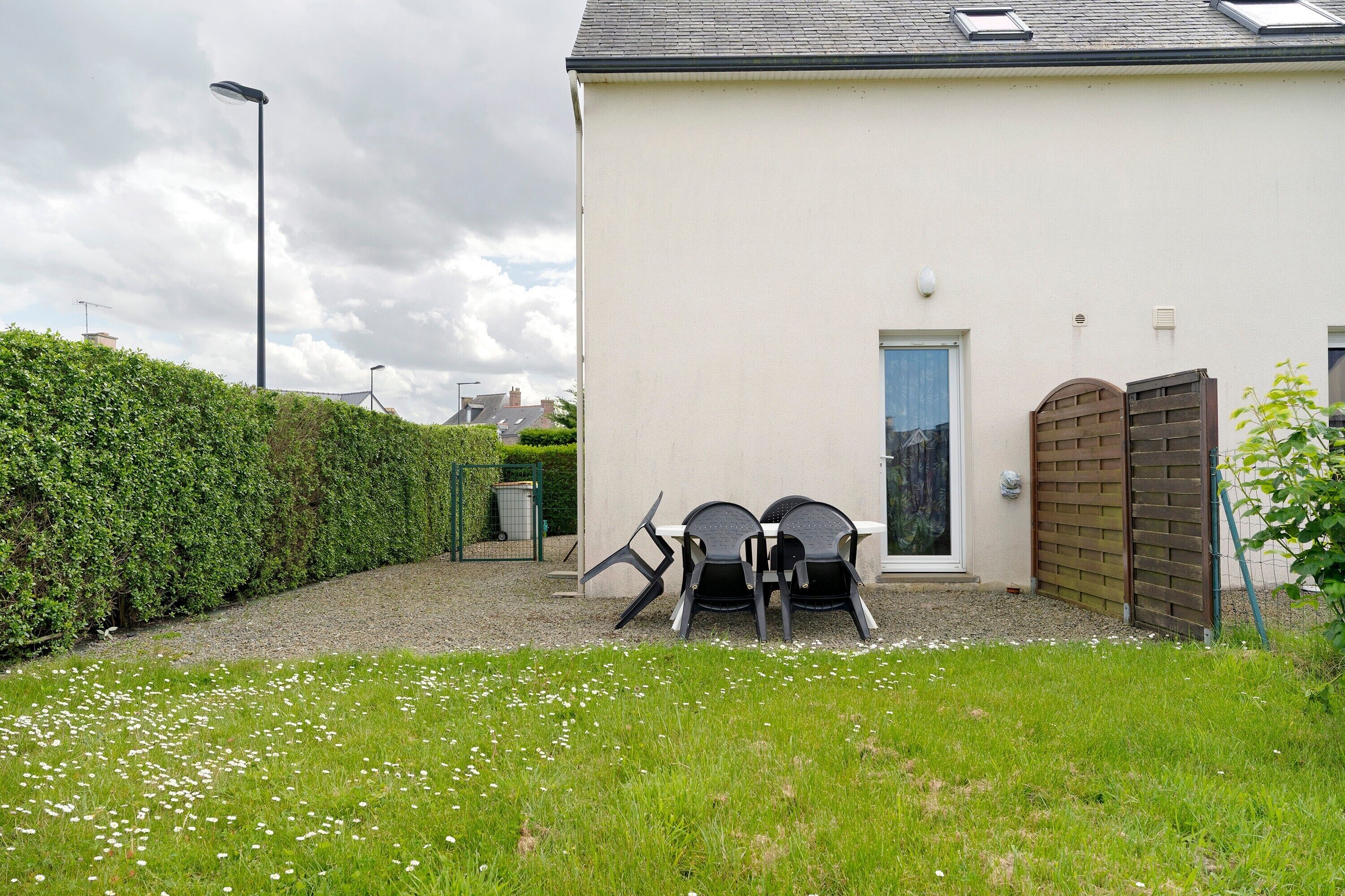 A house with a white exterior, a door, and a small garden area with three chairs and a table.