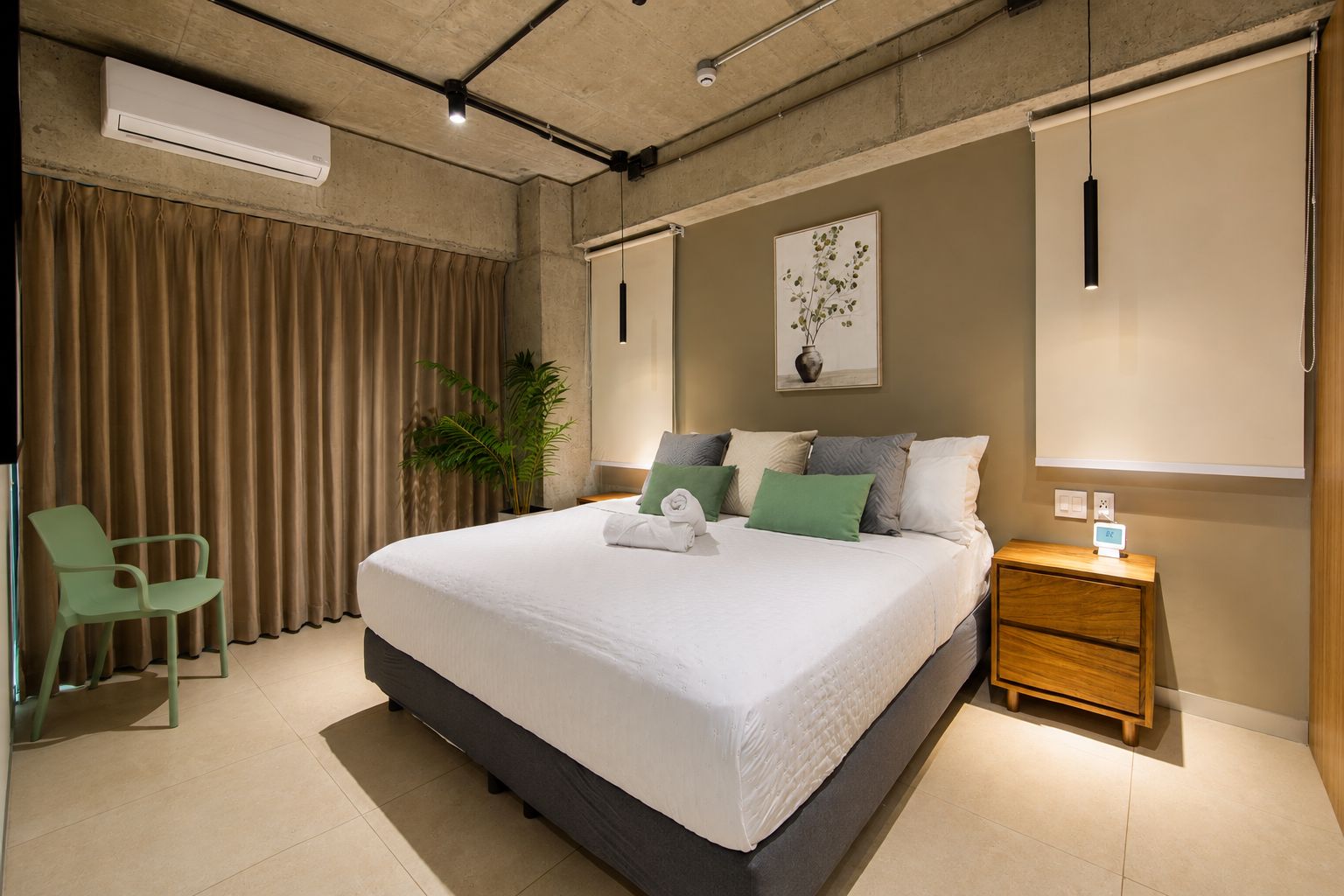 A modern hotel room with a large bed, a desk, a chair, and a potted plant.